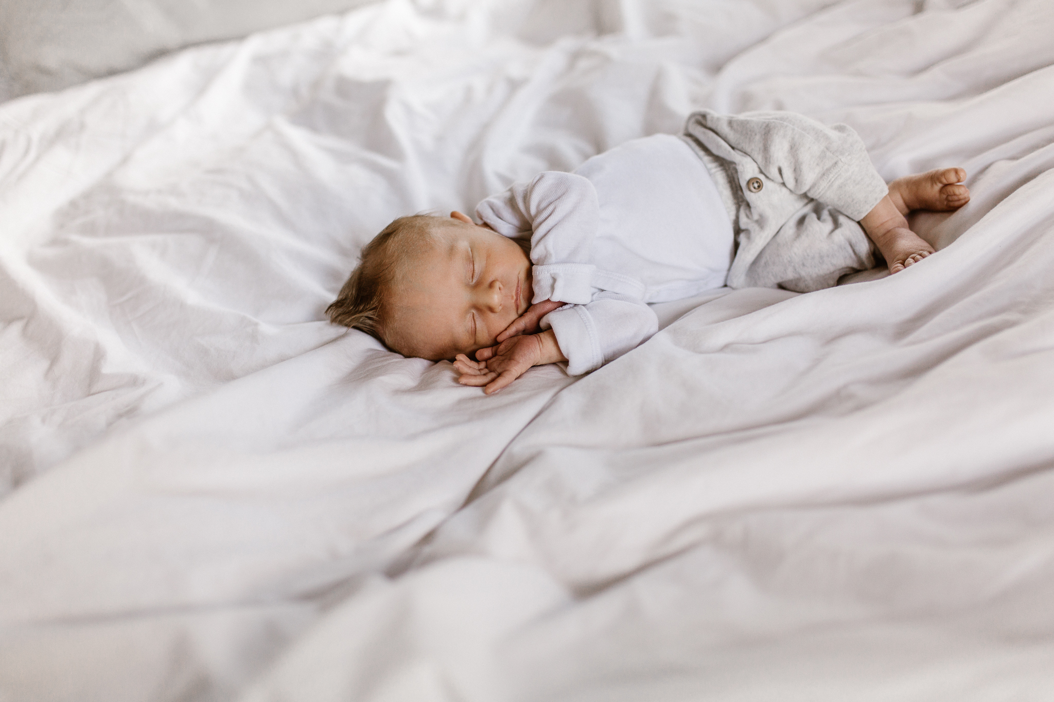 Baby boy cozied up and sleeping on his parent's bed.